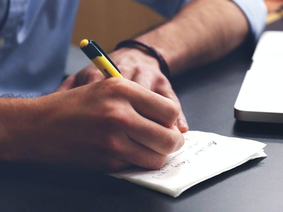 Person Writing on Paper Using Yellow and Black Pen